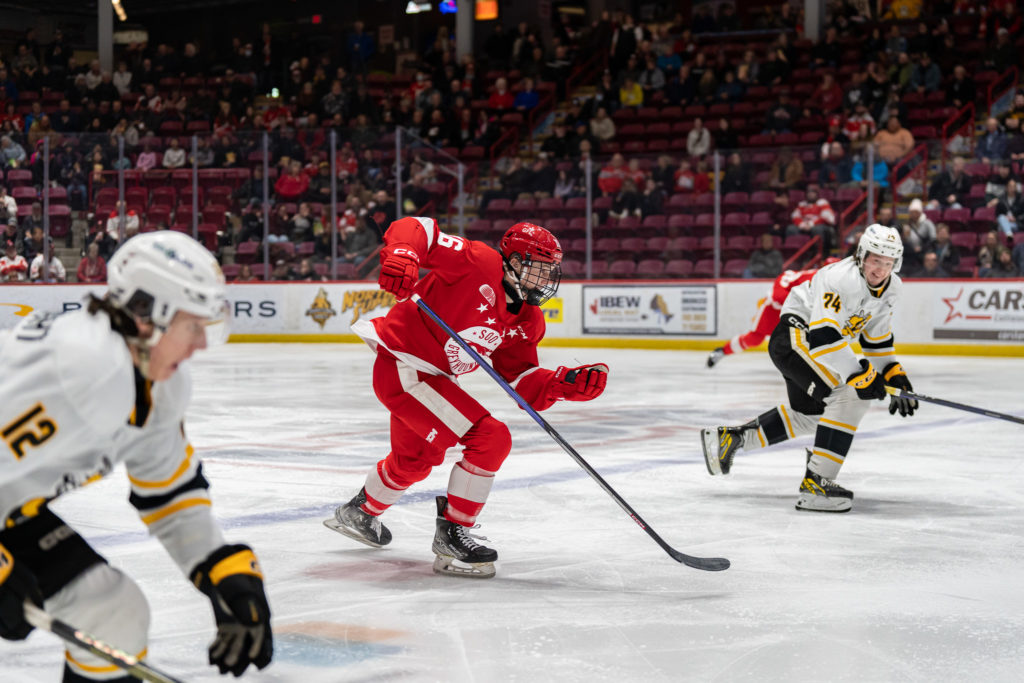 Action shot of Spencer Evans wearing #16 for the Soo Greyhounds and two Sarnia players.